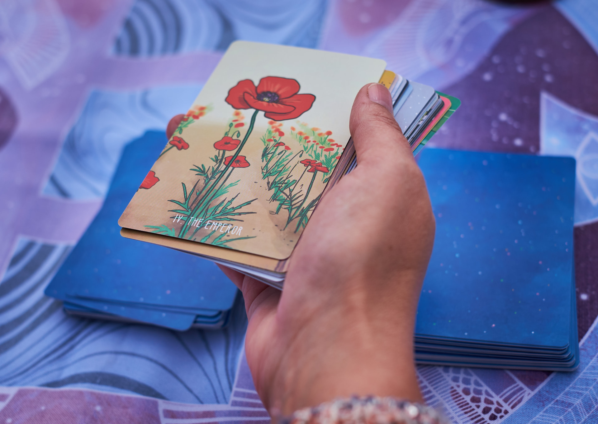 Hand die de tarotkaart De Keizer vasthoudt tegen een diepblauwe achtergrond, uit het tarotspel van Annick Van Damme